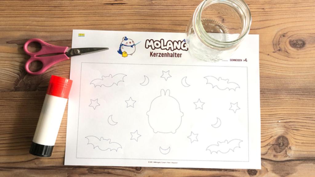 Eine Bastelvorlage, Schere, Kleber und ein Glas auf einem Holztisch