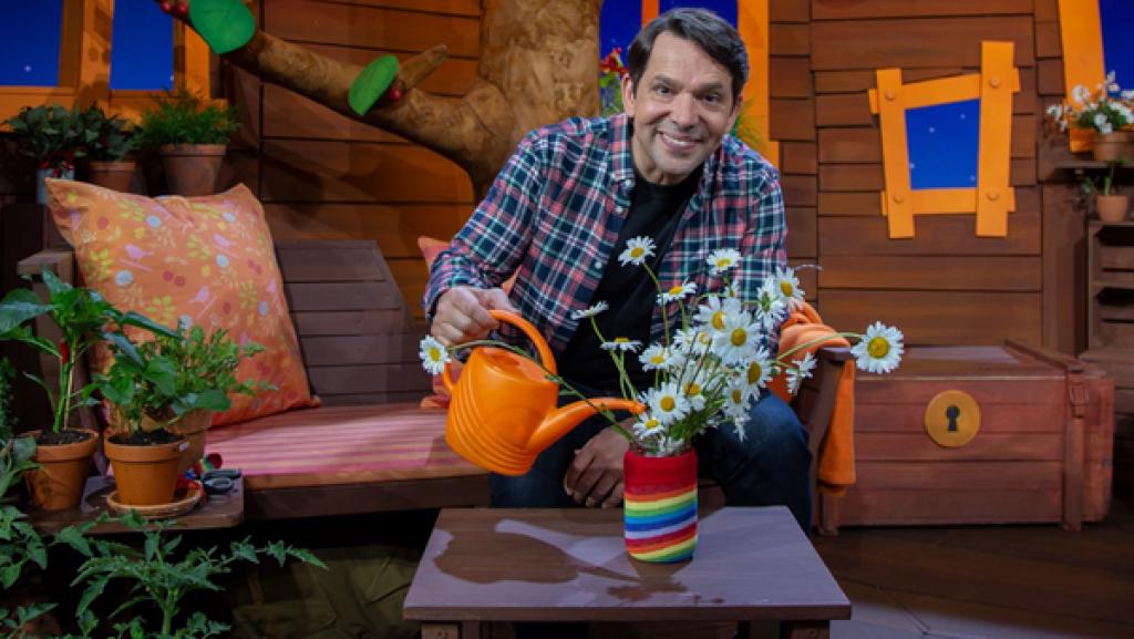 Juri hat Blumen gepflückt und sucht nach einer Vase. Zum Glück findet er ein leeres Marmeladenglas und gestaltet mit Stoffresten und Schleifenband eine schöne Blumenvase.