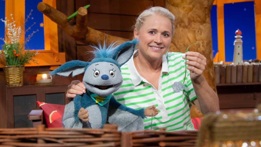 Singa zeigt Fidi, wie sie lustige Geräusche mit einem Grashalm macht.