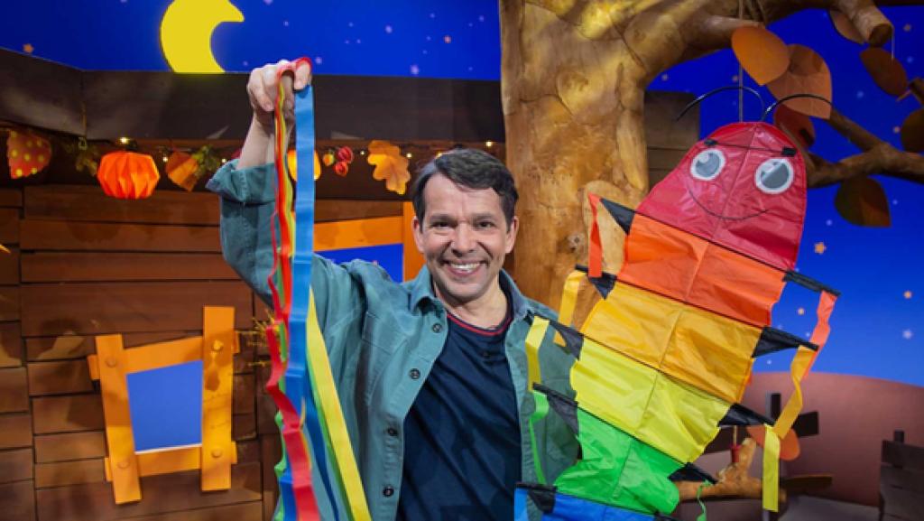 Juri steht im Baumhaus und hält einen bunten Drachen in die Höhe. Der Drachen hat die Form einer Raupe.