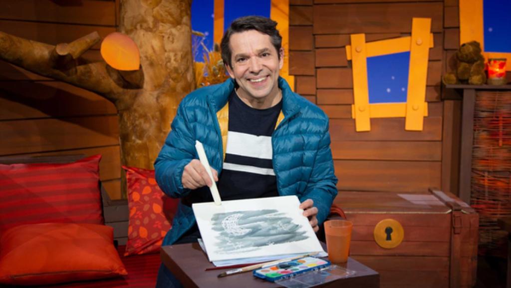 Juri hält ein gemaltes Bild und eine weiße Stabkerze in der Hand. Davor steht ein Wasserfarbkasten.