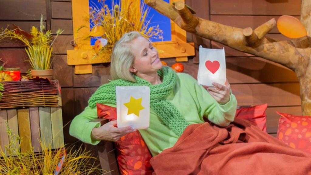 Singa sitzt auf dem Baumhaussofa und hält zwei Papiertüten mit Teelichtern in der Hand.