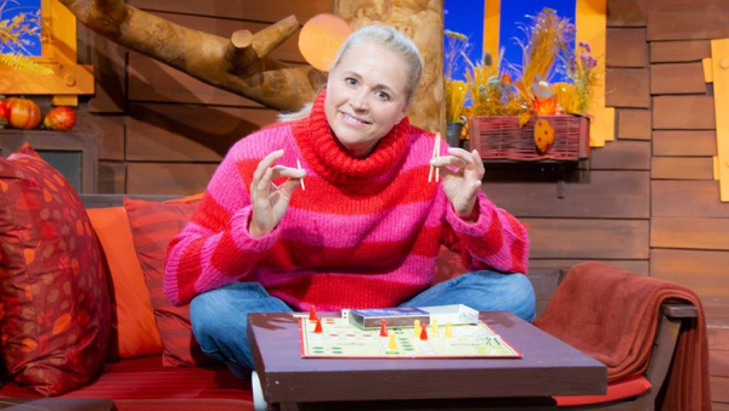 Singa sitzt vor einem Brettspiel. In der Hand hält sie drei unterschiedlich lange Streichhölzer.