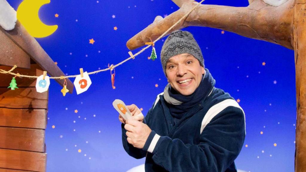 Juri steht vor einer Girlande mit selbst gebasteltem Schmuck und zeigt auf ein Papier.