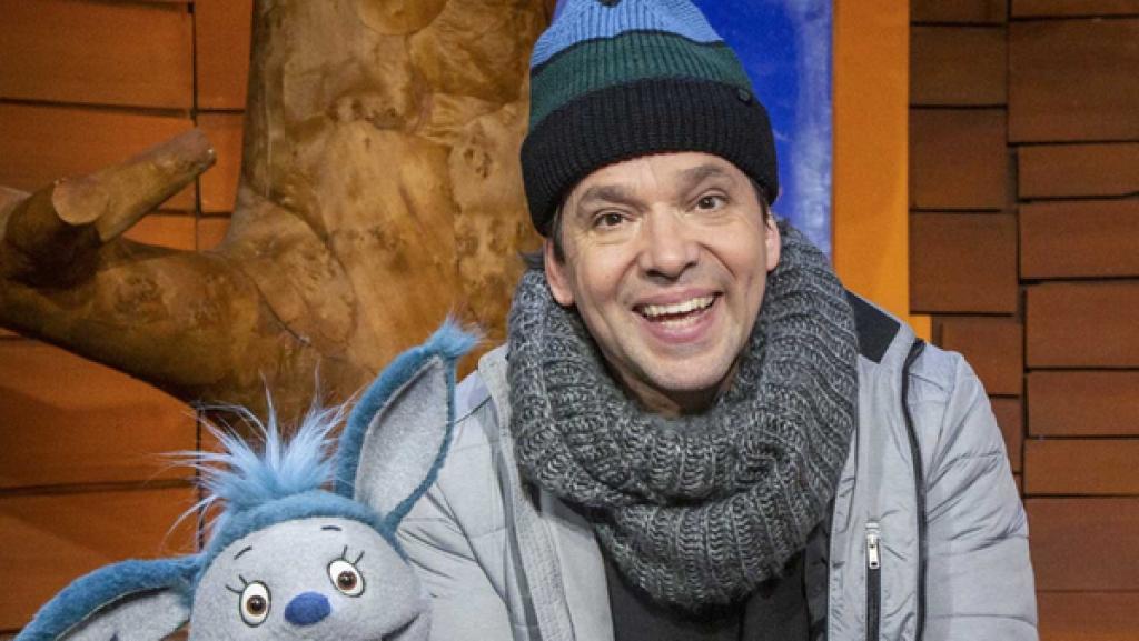 Juri und Fidi sitzen auf dem Sofa im Baumhaus. Juri hält einen Hefekranz in der Hand.