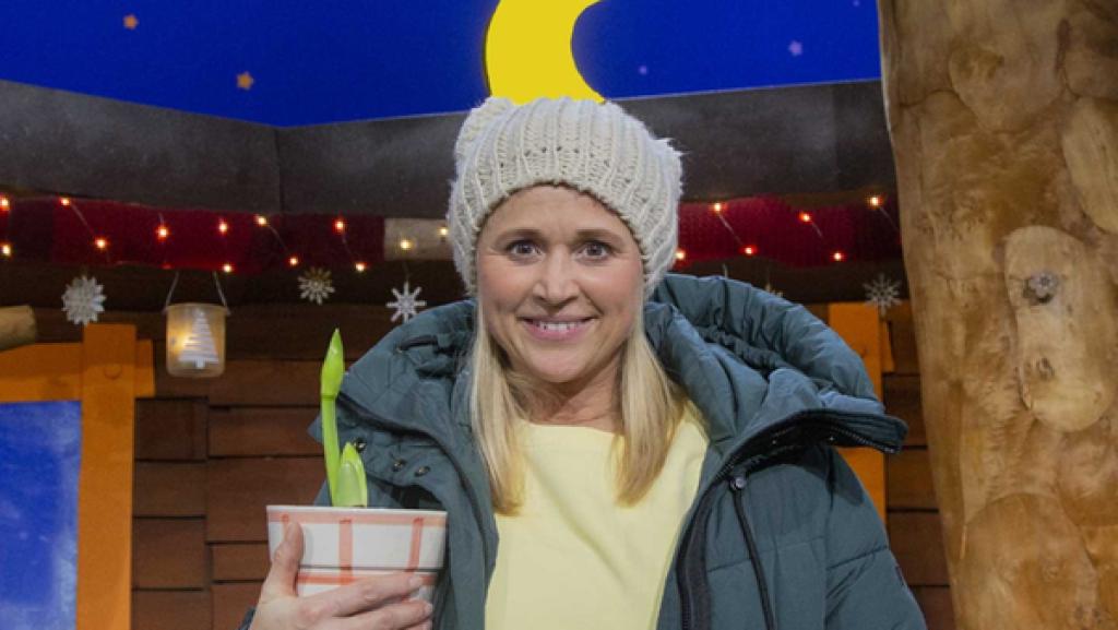 Singa steht im Baumhaus und hält eine Pflanze mit einem Blumentopf in der Hand.