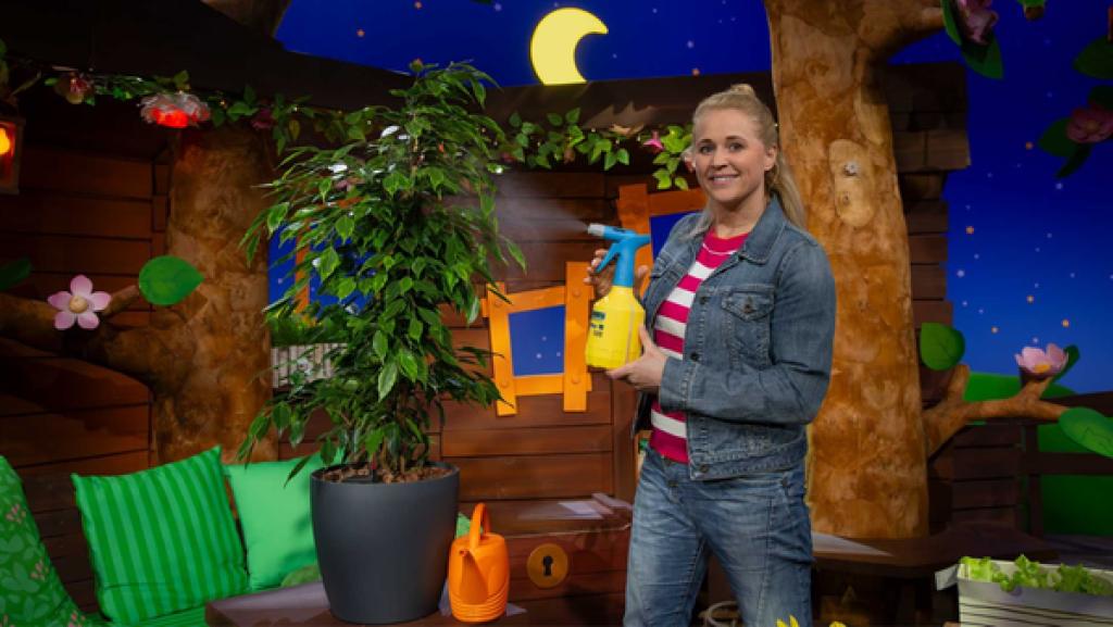 Rechte: KiKA Singa sprüht Wasser auf einen Ficus, der neben ihr steht.