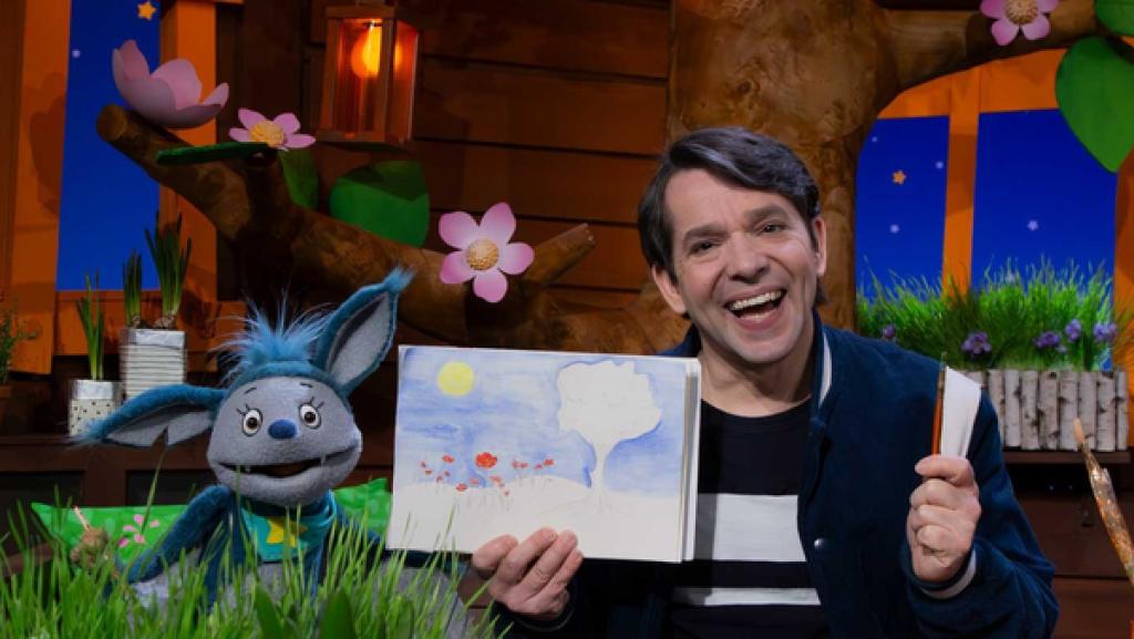 Rechte: KiKA Fidi und Juri sitzen im Baumhaus. Juri hält ein selbst gemaltes Bild hoch. In der anderen Hand hält er einen Pinsel.