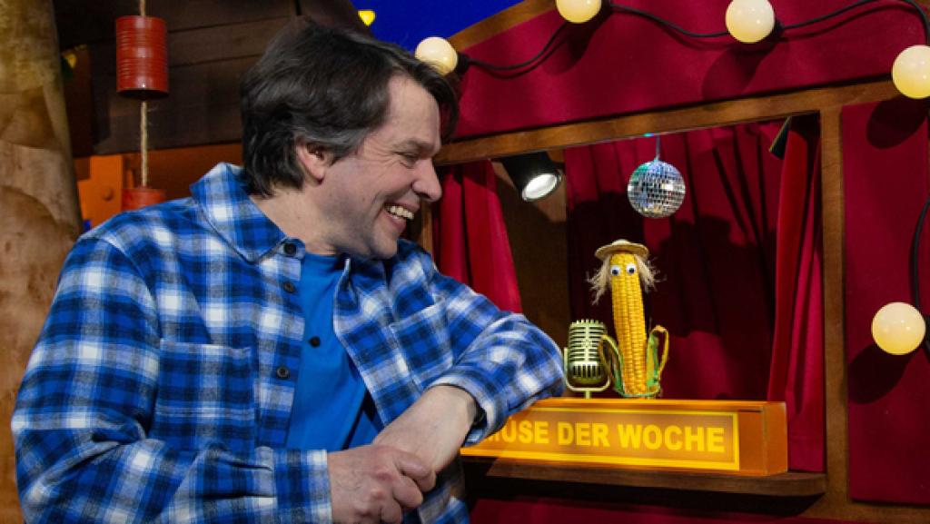 Juri steht neben dem Theater im Baumhaus. Im Theater ist Monty Mais zu sehen.