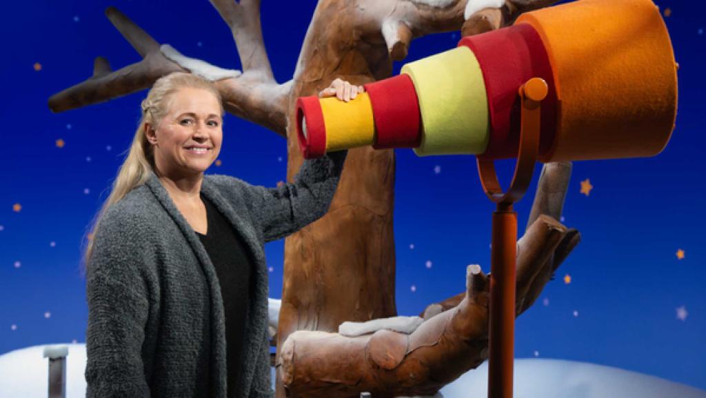 Singa steht am Fernrohr und lächelt.