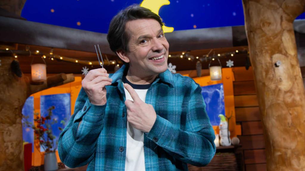 Juri steht lachend im Baumhaus und zeigt mit dem Finger auf eine Stimmgabel.