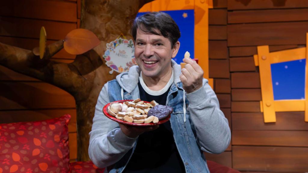 Juri hält lachend eine Plätzchenteller hoch. In der Hand hält er einen Vanillekipferl.