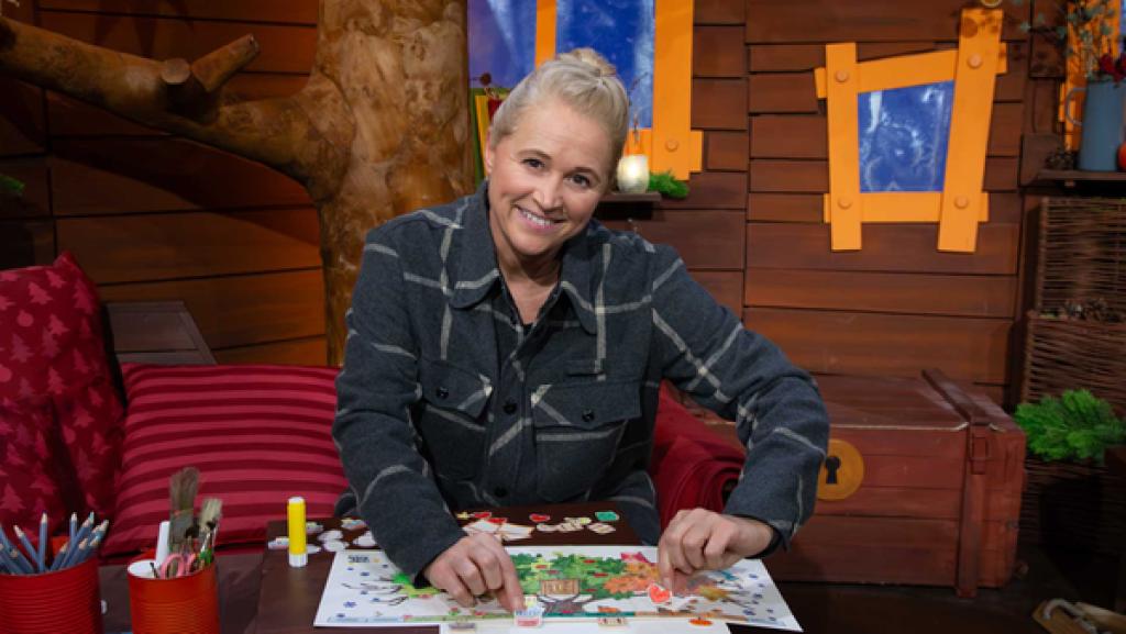 Singa sitzt im Baumhaus. Sie hält zwei ausgeschnittene Symbole aus der Bastelvorlage in der Hand.