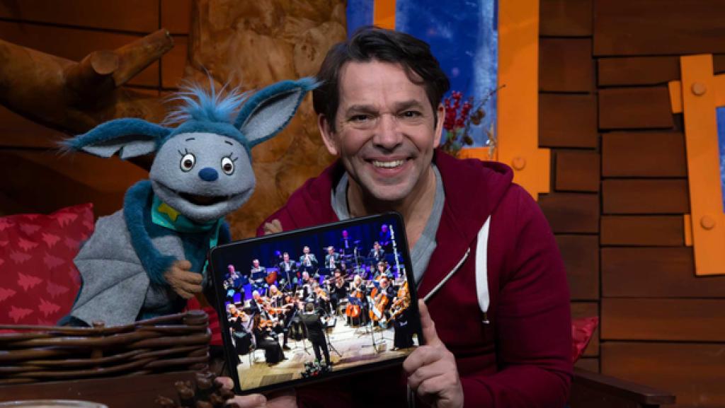 Fidi und Juri sitzen lachend zusammen. Juri hält das Tablet mit einem Orchester-Bild in der Hand.