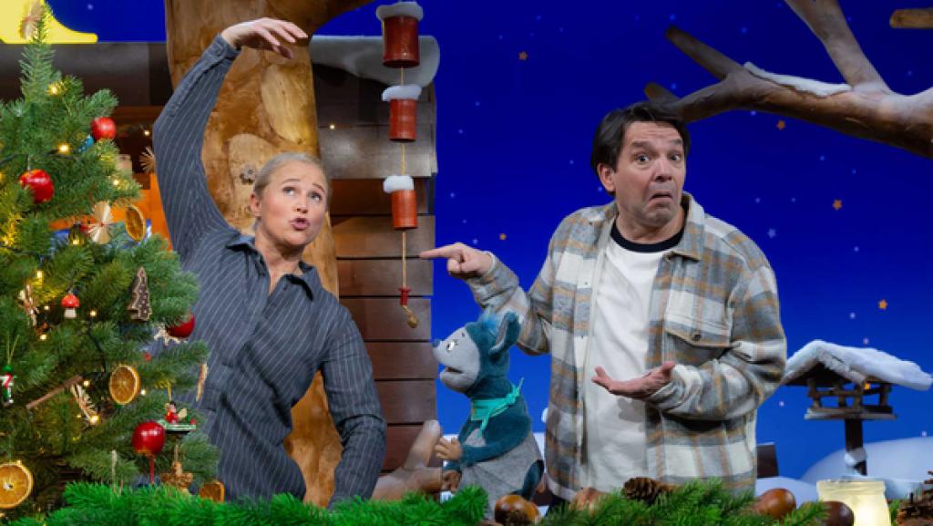 Singa macht eine Pantomime. Fidi und Juri schauen rätselnd. Neben ihnen steht ein Weihnachtsbaum.