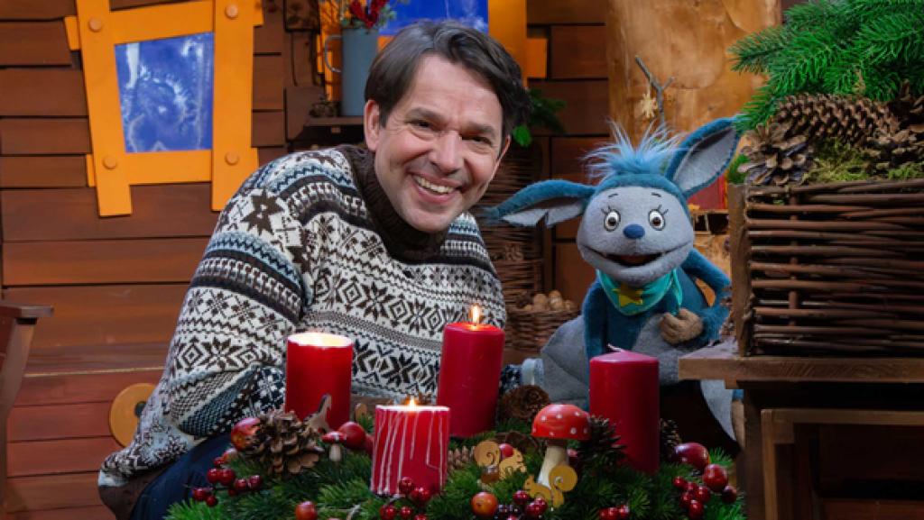 Fidi und Juri sind lachend im Baumhaus und sitzen hinter dem leuchtenden Adventskranz.