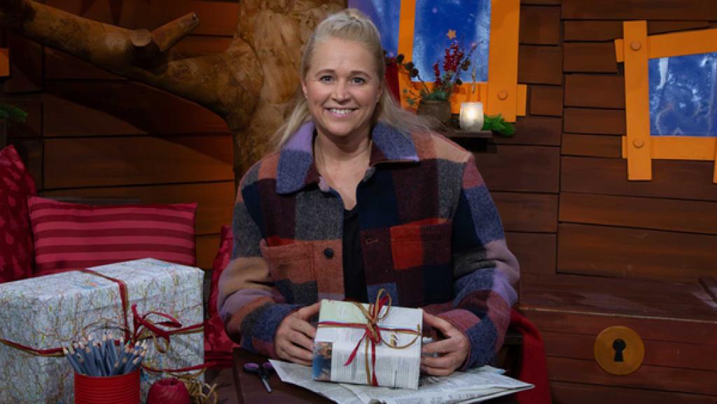 Singa sitzt auf dem Sofa und hält ein in Zeitungspapier gepacktes Geschenk in der Hand.