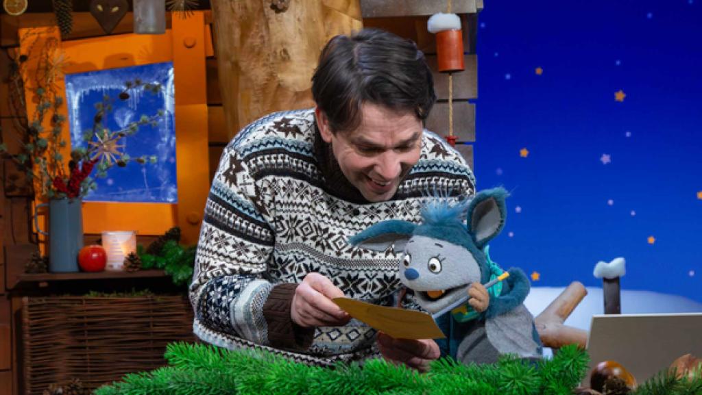 Juri hält lachend einen Zettel in den Händen. Fidi hält einen Stift und malt auf dem Zettel.