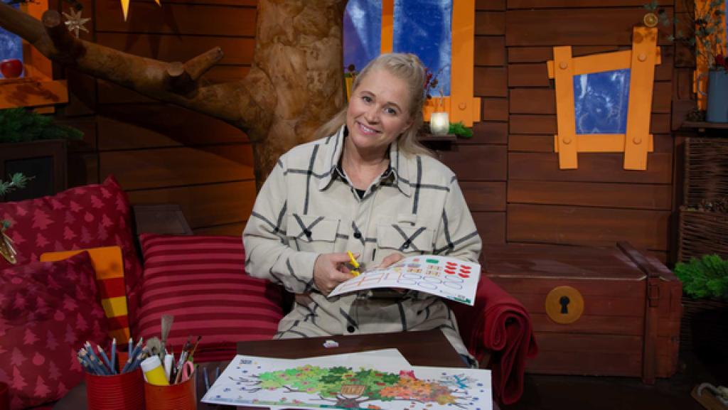 Singa sitzt im Baumhaus. Sie schneidet mit einer Schere in ein Papier aus der Bastelvorlage.