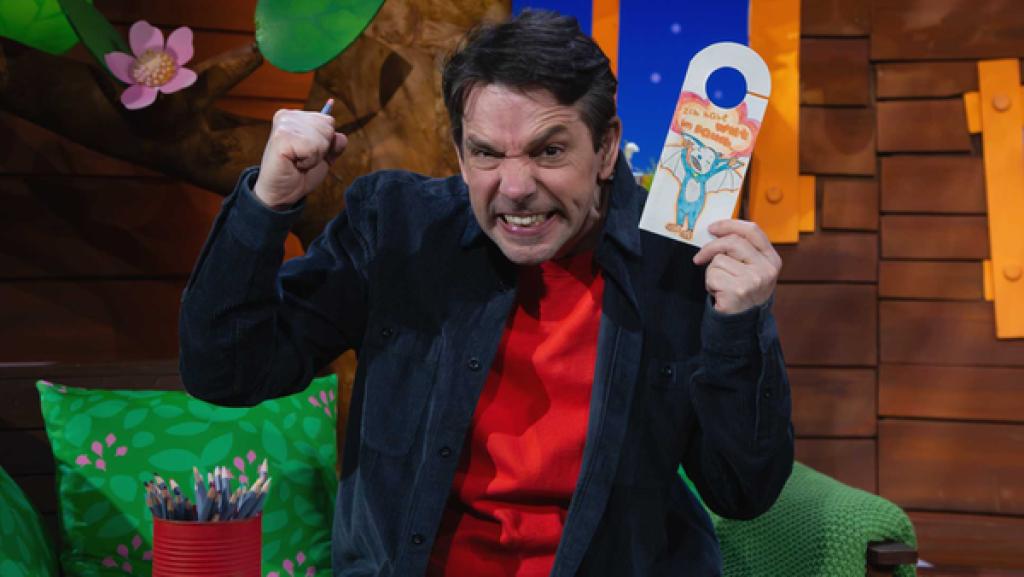 Juri sitzt im Baumhaus und hält das Mach-MiT-Türschild der Wut in der Hand. Dabei guckt er sehr wütend.