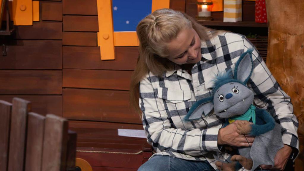 Fidi sitzt auf Singas Schoß im Baumhaus. Singa schaut Fidi an.