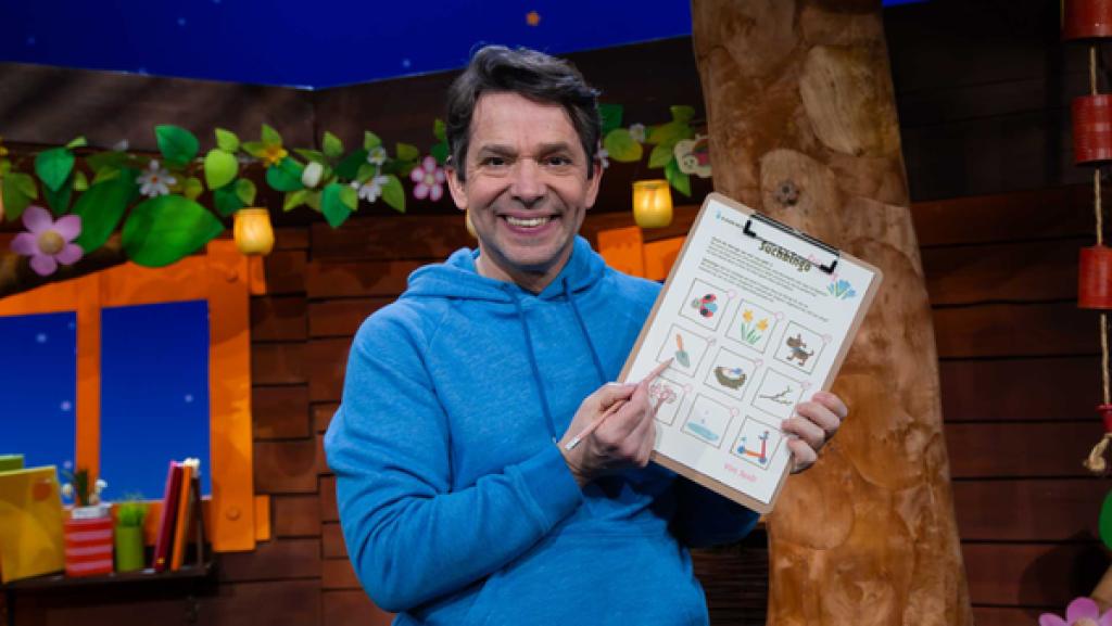 Juri steht im Baumhaus und hält in der Hand ein Klemmbrett mit einem Bingospiel.