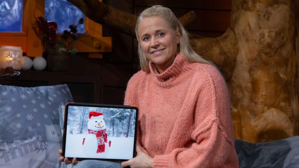 Singa sitzt im Baumhaus und zeigt auf dem Tablet ein Bild von einem Schneemann.