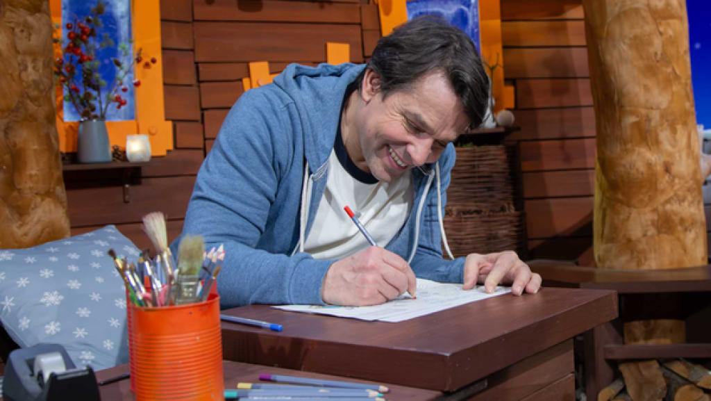 Juri sitzt im Baumhaus und malt mit einem Stift die MACHMiT!-Bastelvorlage aus.