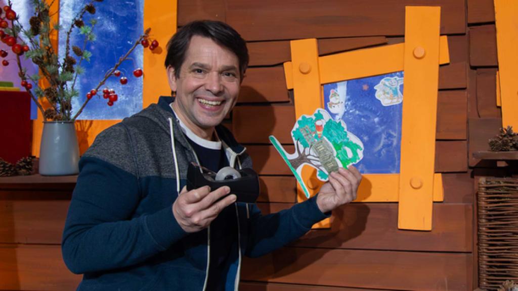 Juri sitzt auf der Schatzkiste im Baumhaus und klebt lachend die MACHMiT!-Fensterbilder an.