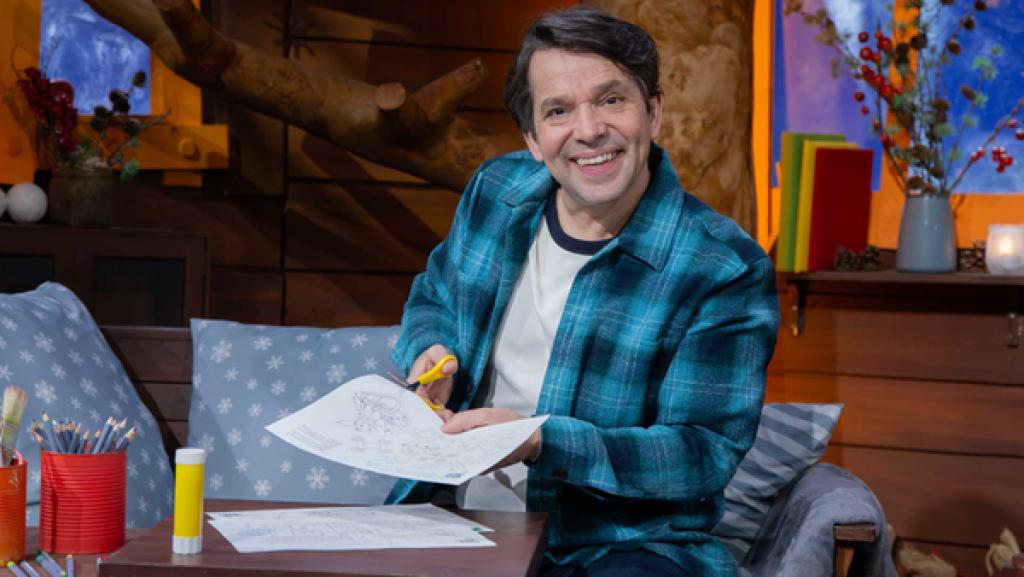 Juri sitzt lachend im Baumhaus und schneidet mit der Schere in die MACHMiT!-Bastelvorlage.