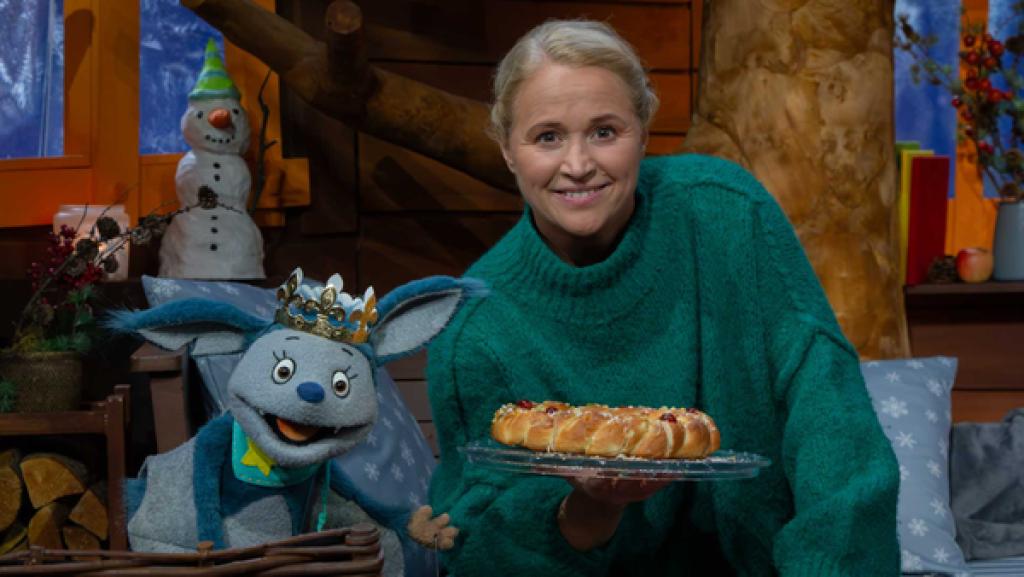 Fidi sitzt mit einer Krone auf dem Kopf neben Singa, die einen Hefekranz in der Hand hält.