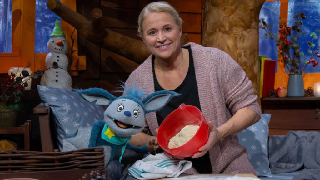 Singa hält eine Schüssel mit Hefeteig in der Hand, Fidi schaut freudig.