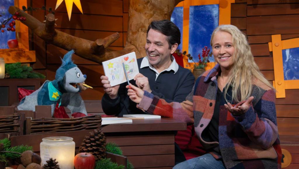 Fidi, Singa und Juri sind im Baumhaus. Juri hält ein Bild hoch. Fidi und Singa halten einen Stift. 