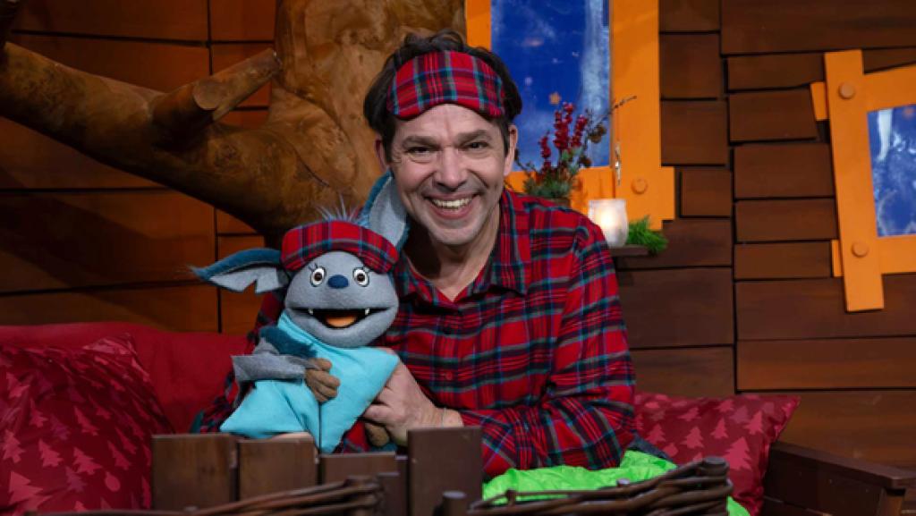 Juri und Fidi sitzen auf dem Sofa. Sie tragen rot karierte Schlafanzüge und Schlafmasken.