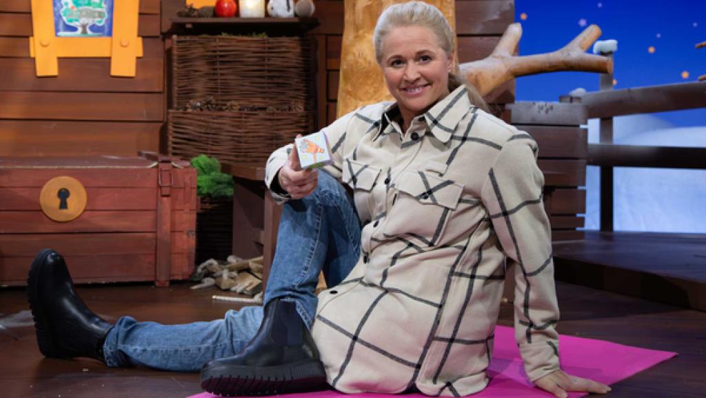 Singa sitzt auf dem Boden im Baumhaus auf einer rosa farbenen Sportmatte und hält den Ruhewürfel in der Hand.