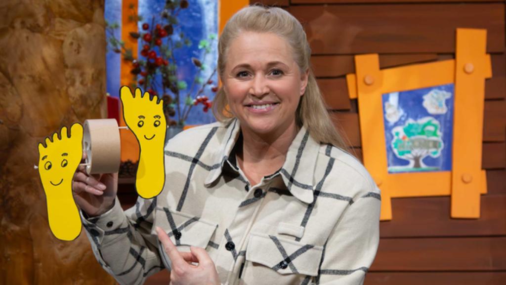 Singa hält eine lustige Bastelei mit Füßen aus Papier und einer Rolle Klebeband hoch.