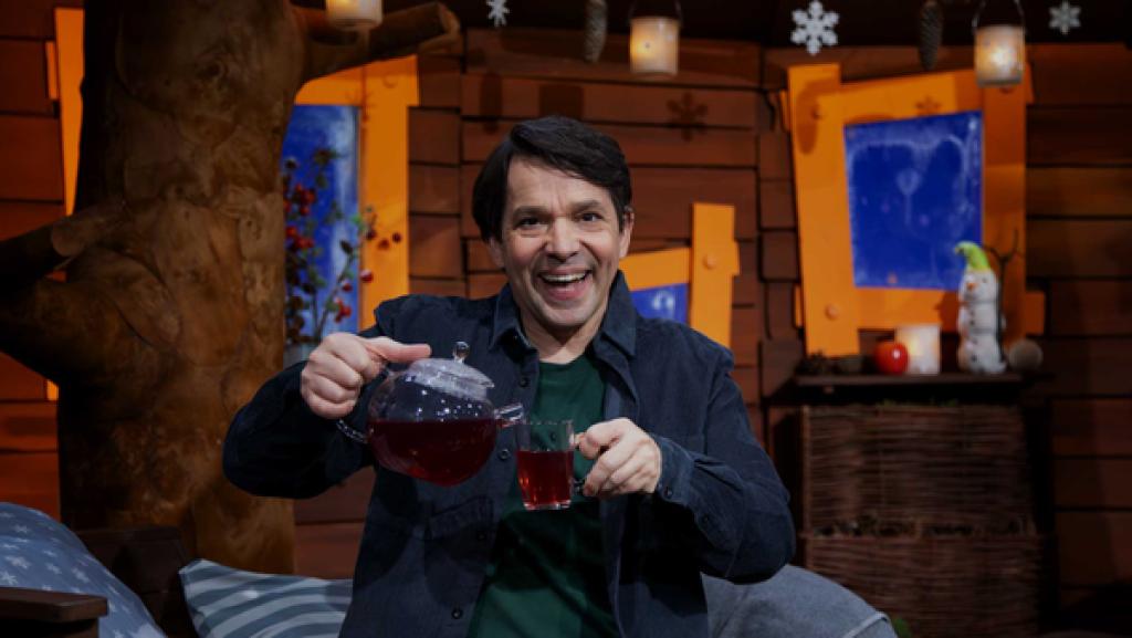 Juri hält eine Teekanne und eine Teetasse in der Hand. Er lächelt.