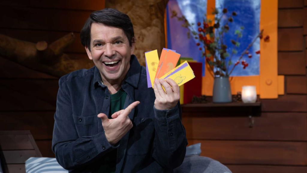 Juri sitzt im Baumhaus und hält bunte Karten mit Symbolen in der Hand.