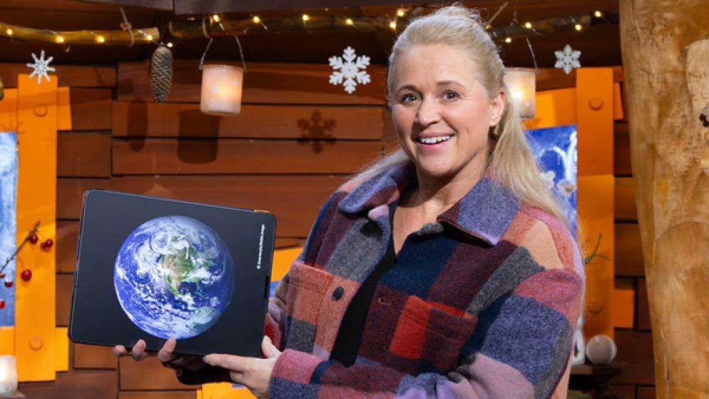 Singa hält lächelnd das Tablet in den Händen, auf dem ein Bild von der Erde zu sehen ist.