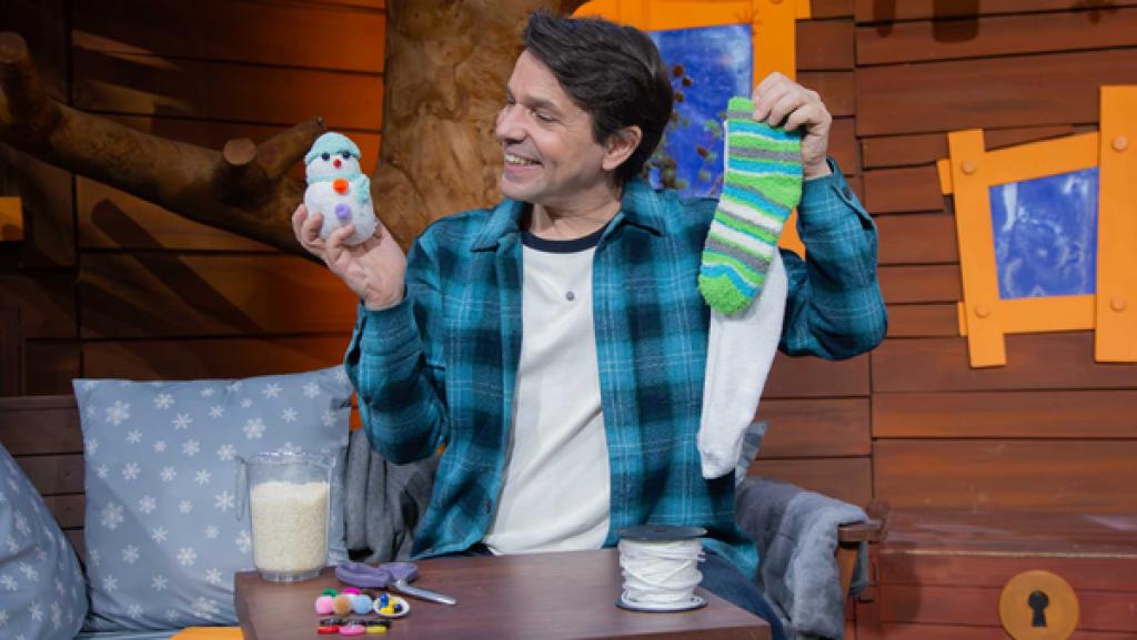 Juri schaut lachend auf einen gebastelten Schneemann in seiner Hand. In der anderen hält er Socken.