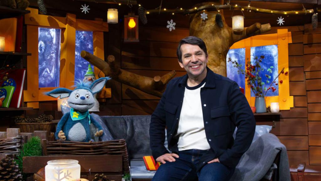 Fidi und Juri sitzen auf dem Sofa im Baumhaus. Sie lächeln beide.