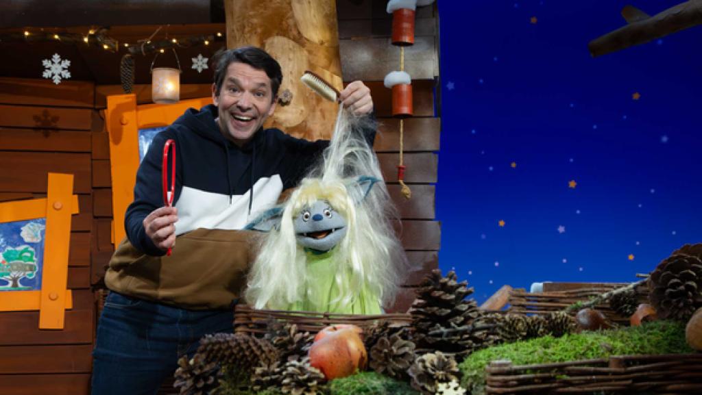 Fidi trägt eine blonde Perücke. Juri hält ihre Haare in die Höhe und einen Spiegel in der Hand.