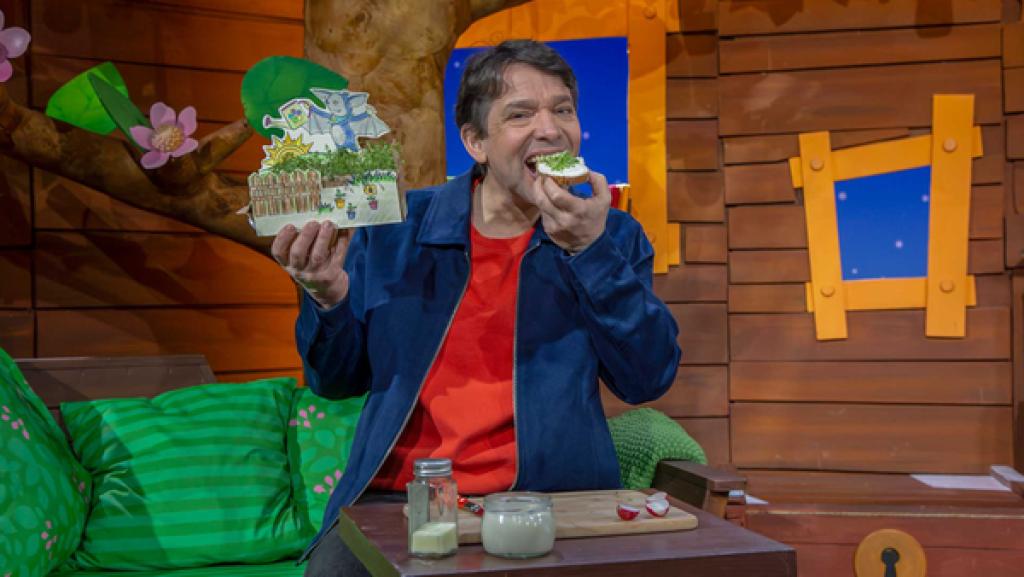 Juri sitzt im Baumhaus und hält einen Fidi-Garten in der Hand. Er isst ein Kresse-Brot.