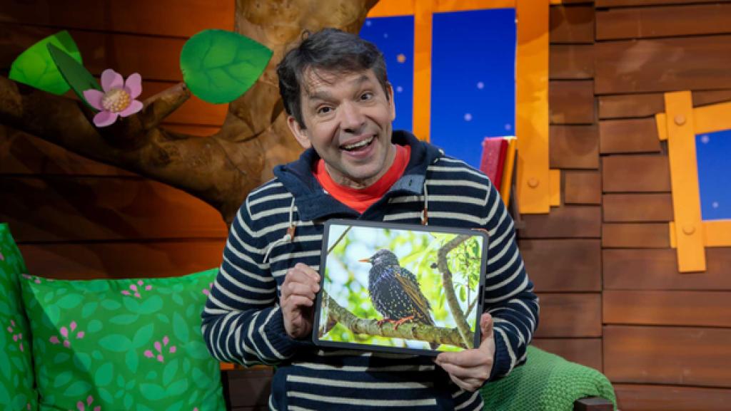 Juri sitzt im Baumhaus und hält das Tablet, auf dem ein Vogel-Bild zu sehen ist.