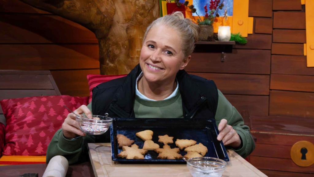 Singa sitzt am Tisch und hat ein Backblech mit Keksen in der Hand.