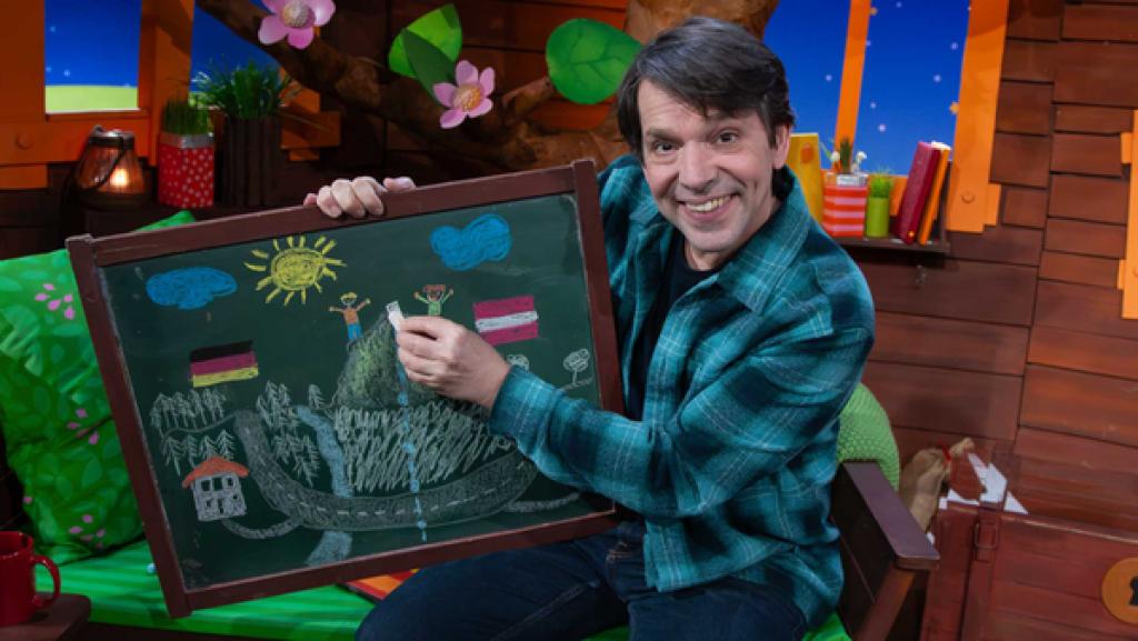 Juri sitzt im Baumhaus mit einer Kreidetafel.