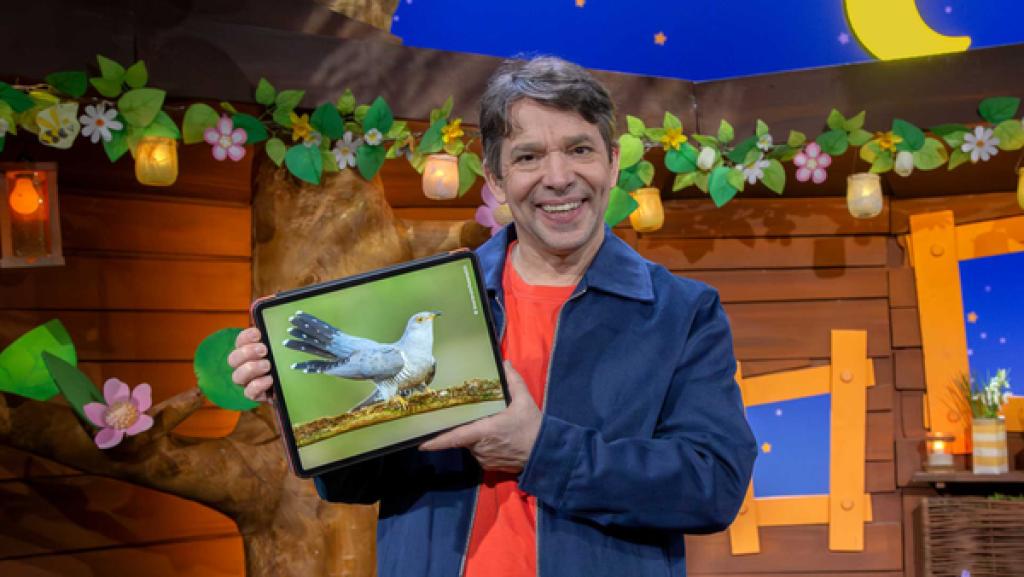 Juri steht im Baumhaus und hält das Tablet, auf dem ein Bild vom Kuckuck zu sehen ist.