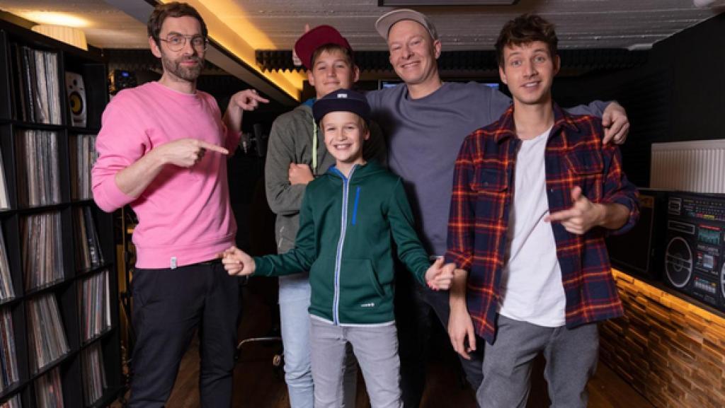 Die "Dein Song" Kandidaten Anton und Fabian stehen zwischen ihren drei Musikpaten "Deine Freunde" und lächeln. Die Musikpaten zeigen mit ihren Zeigefinger auf die beiden Kandidaten, die eine Cap aufgesetzt haben. Alle lächeln.