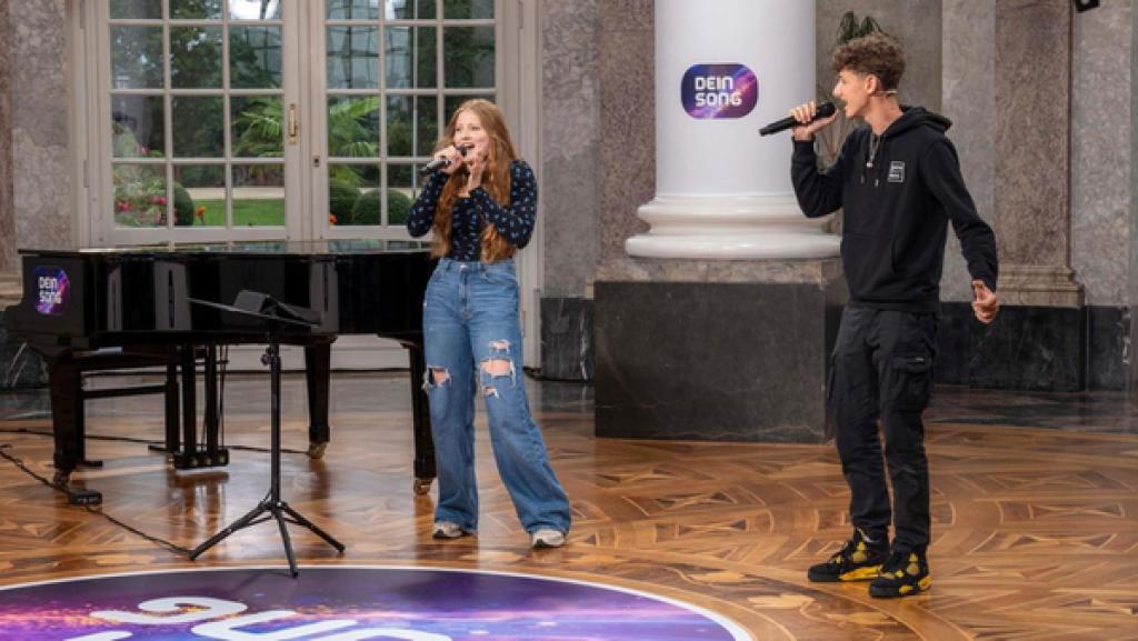 Das Das Songwriting Duo Lisa und Lukas (v.l.n.r) stehen auf der "Dein Song" Bühne, halten ein Mikrofon in der Hand und singen.