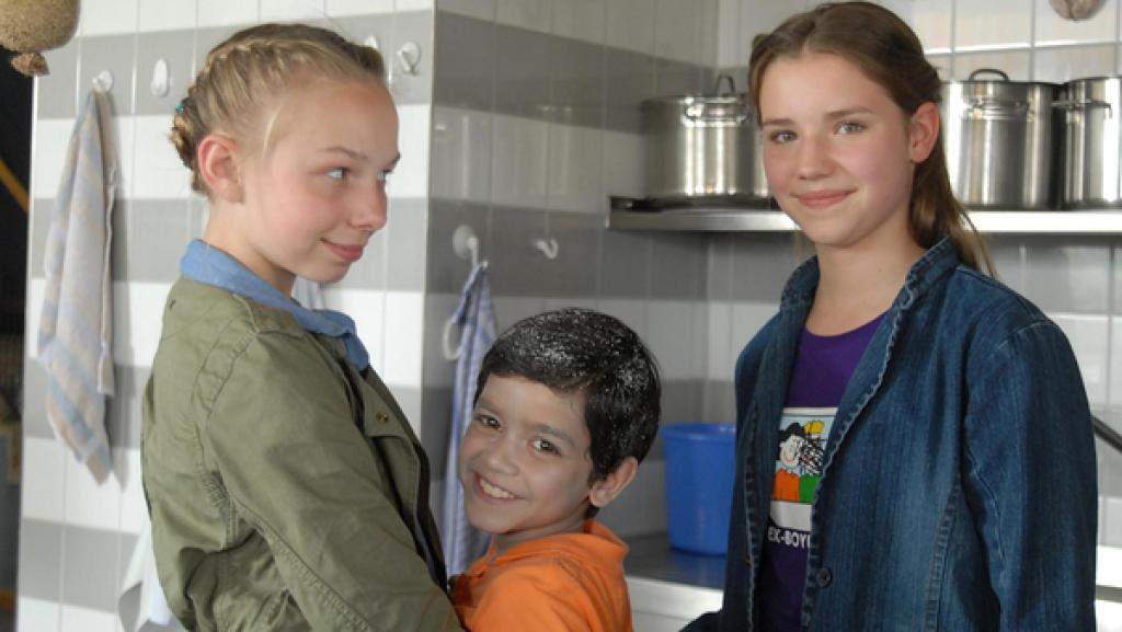 Jessi, Luis und Nina (Martha Fries, Emilio Sanmarino und Carolin Garnier) stehen lächelnd in einer Küche.